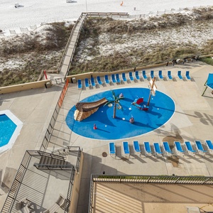 The pool area features a vibrant splash pad with a pirate ship theme, surrounded by lounge chairs and a shaded gazebo