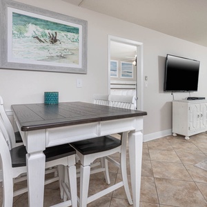 This inviting living area features a sleek TV, a stylish dining table, and a stunning beach view through large windows