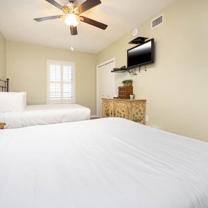 Rest in this guest bedroom featuring two queen beds, a TV, and natural light from the window for a relaxing stay