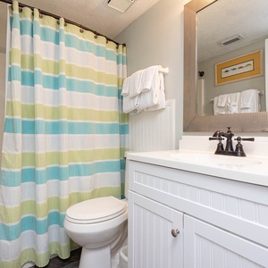The master bathroom features a striped curtain, a sleek vanity with a large mirror, and fresh towels for a refreshing stay