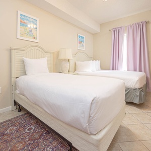 Guest bedroom featuring two twin beds, a light wood dresser, and soft purple curtains, creating a relaxed vacation vibe