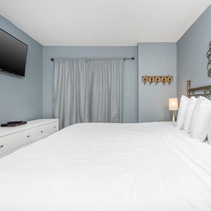 This bedroom features a plush white bed, a sleek TV mounted on the wall, and decorative accents for a relaxing atmosphere