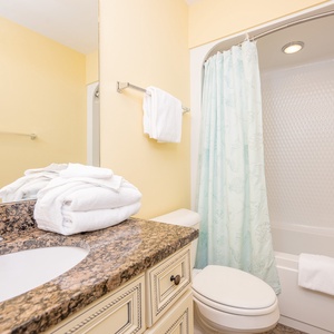 Guest bathroom featuring a granite countertop, fresh towels, and a relaxing tub/shower combo with a sea-themed curtain