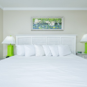 Rest comfortably in this guest bedroom featuring a king bed, bright linens, and cheerful coastal artwork above