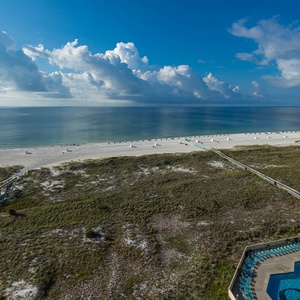 Relaxing view of the tranquil gulf, white sand beach, and inviting pool area framed by lush greenery and beach walkways