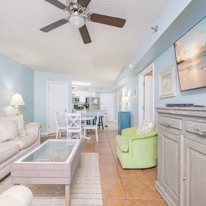 Living space featuring a cozy sofa, vibrant green chair, and a large TV showcasing a beach scene