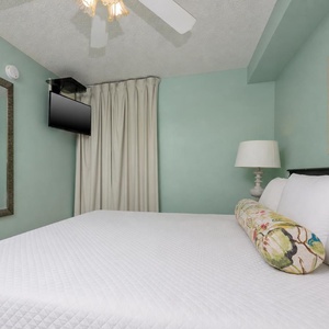 Rest in the serene bedroom featuring a king bed, flat-screen TV, and calming teal walls for a peaceful retreat