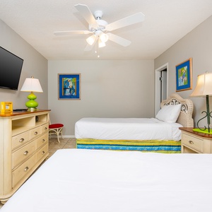 This guest bedroom features two beds with colorful bedding, a mounted TV, and cheerful decor, perfect for a relaxing stay