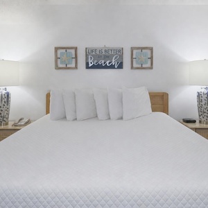 A king bed with white linens is flanked by blue and white lamps, complemented by beach wall art