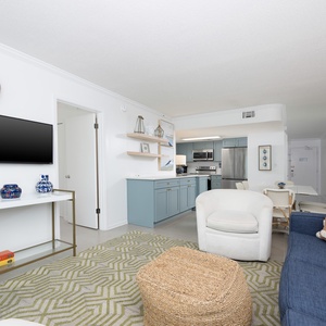 This living area features a sleek TV, colorful decor, and a cozy vibe with a view of the inviting kitchen space