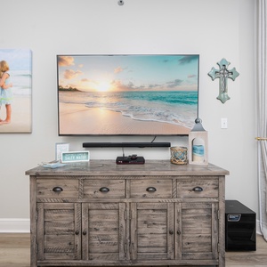 Coastal decor enhances the living area, featuring a TV, wooden cabinet, and access to a balcony with a view of the gulf