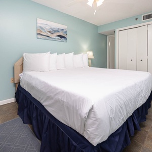 The guest bedroom features a king bed with crisp white linens, a light blue accent wall, and a stylish dresser for storage