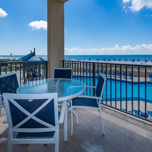Enjoy a relaxing outdoor dining space with a glass table and chairs, overlooking the pool area and beach beyond