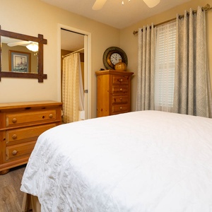 Warm wooden furniture complements the inviting atmosphere of this guest bedroom, featuring a queen bed and soft natural light