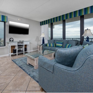 The living area features a comfortable couch and stunning views of the beachfront through large windows