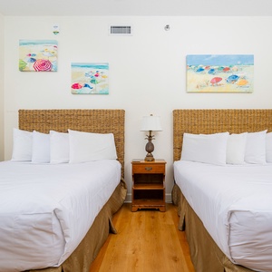 Brightly decorated guest room features two comfortable double beds with woven headboards and beach art on the walls