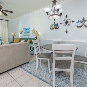 Brightly decorated living area features a cozy sofa, dining table, and large windows offering a glimpse of the beach