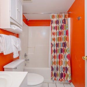 The master bathroom features a vibrant red wall, colorful circular shower curtain, and ample storage for a refreshing stay