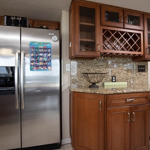 Sleek kitchen features a stainless refrigerator, granite countertops, and a wet bar with wine storage and glassware