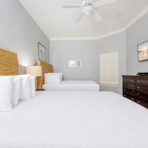 Comforting guest bedroom featuring two queen beds, a flat-screen TV, and stylish woven headboards