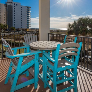 Bright turquoise seating surrounds a round table on the balcony, offering a view of the beach and nearby palm trees