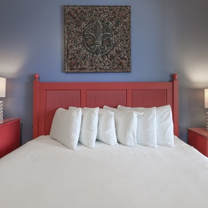 The master bedroom features a vibrant red bed frame, king bed, soft white linens, and stylish lamps