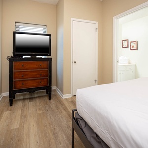 Guest bedroom featuring two double beds, a wooden dresser with a TV, and a view into a nearby bathroom with fresh towels