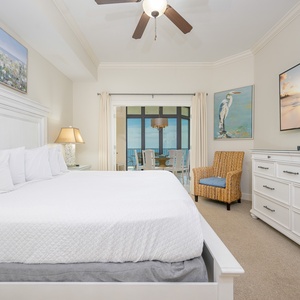 Elegant master bedroom featuring a king-size bed, warm lighting, and a view of the inviting dining area and balcony beyond