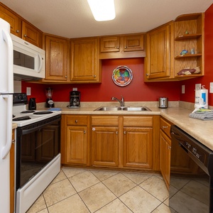 Cozy kitchen featuring warm wooden cabinets, essential appliances, and a vibrant red accent wall for a welcoming atmosphere