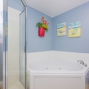 The master bathroom features a relaxing jetted tub, a glass shower, and cheerful beach-themed decor on soft blue walls