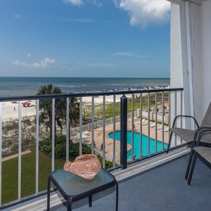 Enjoy a stunning beachfront view from the balcony, featuring two chairs and a decorative shell on the table