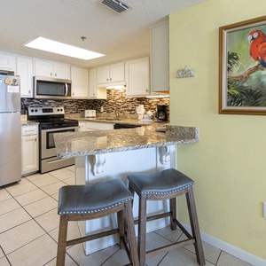 A modern kitchen features stainless appliances, a stylish countertop, and a vibrant parrot painting above the breakfast bar