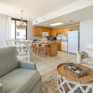 Seating area features a soft blue sofa and a charming wooden coffee table, with a dining space and kitchen in view