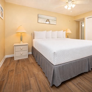 A bright guest bedroom features a king bed with decorative pillows, nightstands with lamps, and warm yellow walls