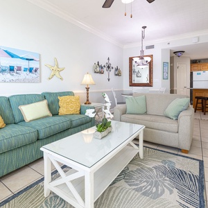 Living area features a teal sofa with queen sleeper, a glass coffee table, and a view into the adjacent dining space