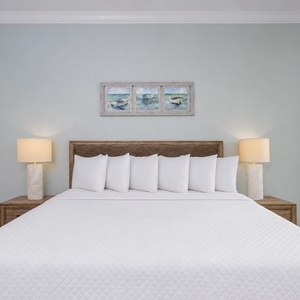 Seven plush pillows line the king guest suite bed where peaceful quiet invites restful sleep by the coast view window