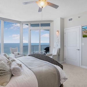 The master bedroom features direct balcony access, a TV, and a stunning view of the beach from large windows