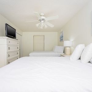 Bright guest bedroom featuring two queen beds, a flat-screen TV, and coastal art, creating a serene and inviting atmosphere