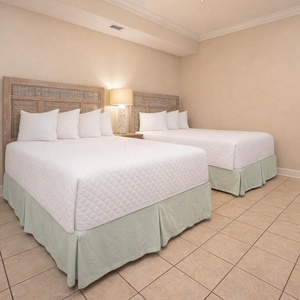Guest bedroom featuring two plush double beds with decorative pillows and soft green accents