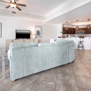 This living area features a blue sectional, a wall-mounted TV, and a stylish kitchen with dark cabinetry and pendant lighting