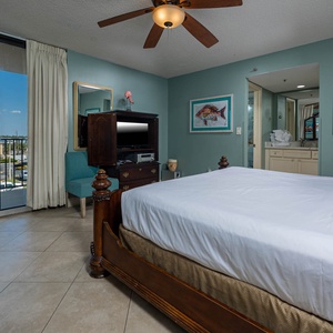 This cozy master suite features a wooden king bed, a TV, vibrant artwork, and a lovely view from the balcony