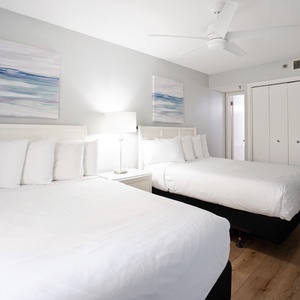 Bright guest bedroom featuring two double beds, stylish artwork, a bedside lamp, and ample space for a comfortable stay