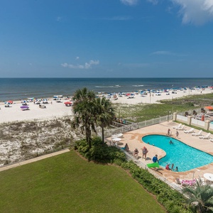 This inviting view showcases a sparkling pool area surrounded by lush greenery, with a beautiful beachfront just steps away