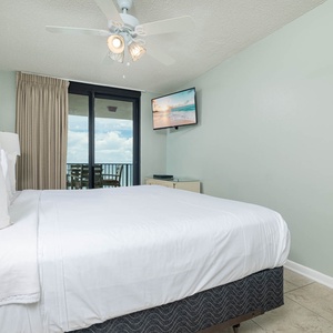 Serene master suite with a king bed, a TV, and a view of the balcony for enjoying the sights and sounds of the beach