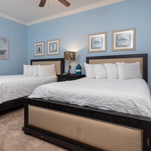 This guest bedroom features two queen beds with white linens, a calming blue wall, and nautical decor for a relaxing stay