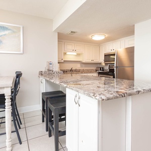 This kitchen features sleek stainless appliances, granite countertops, and a cozy dining area with stylish black chairs