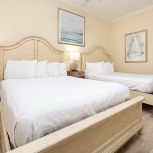 This guest bedroom features two light queen beds, a cozy lamp, and nautical decor, creating a serene retreat for relaxation