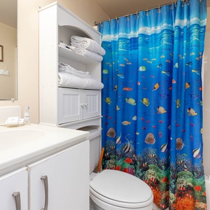 The master bathroom features a vibrant underwater-themed shower curtain, fresh towels, and a clean, bright vanity area