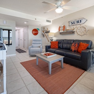 The living area features a cozy sofa with a queen sleeper, beach decor, flat-screen TV, and a lovely view through the window