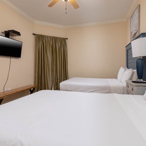 This guest bedroom features two comfortable beds, a wall-mounted TV, and soft green curtains for a relaxing atmosphere